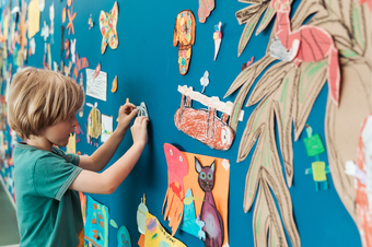 Young boy sticks a colourful drawing to a blue wall