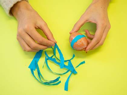 Strips of blue paper being applied to the glue-covered egg