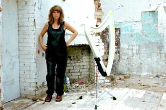 Image of musician Serafina Steer standing in black clothing next to a harp