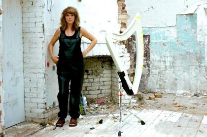 Image of musician Serafina Steer standing in black clothing next to a harp