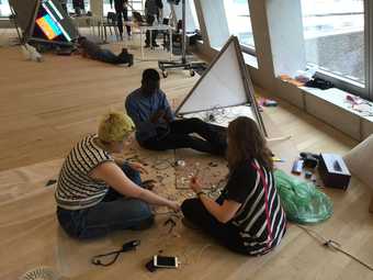 three people sit on the ground and make robots