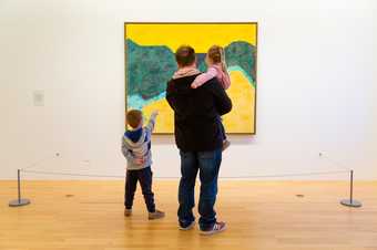 An adult and two young children looking at a painting.