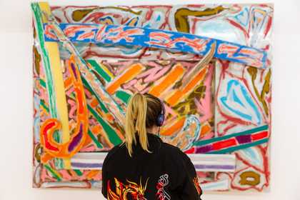 Visitor looking at a colourful abstract painting by Frank Stella in the Constellation display at Tate Liverpool