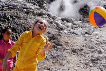 Film still from Mikhail Karikis's Children of Unquiet showing a girl in yellow jacket playing with a beach ball inside a crater