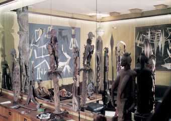 Wifredo Lam surrounded by his collection of African and Oceanic sculptures in the music room in Albissola, 1974