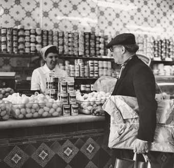Scottie Wilson wearing his tweed cap while shopping at Sainsbury’s, 1964, photographed by Ida Kar