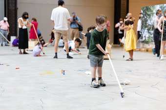 A boy draws on the floor of the Turbine Hall using a pen on a stick