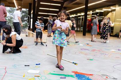 A girl stands in front of others drawing on the Turbine Hall floor