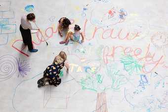 Photo of Turbine hall commission: People drawing with coloured pencils on a large white paper covered floor
