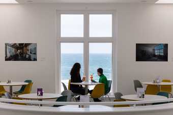 a person and a child sit in the cafe looking out to sea