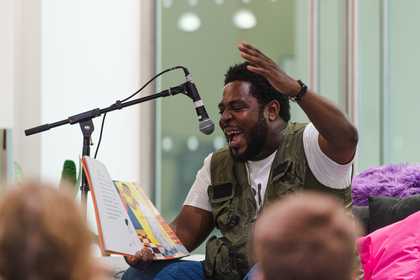 A man sitting down talks into the microphone in front of seated children