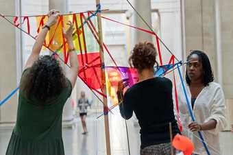 Three people building a colourful sculpture in Tate Britain