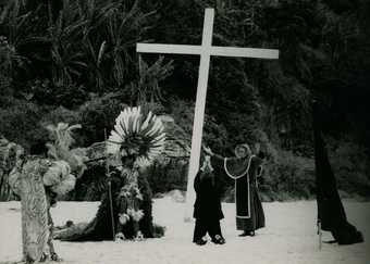 men stands next to a wooden cross on a beach