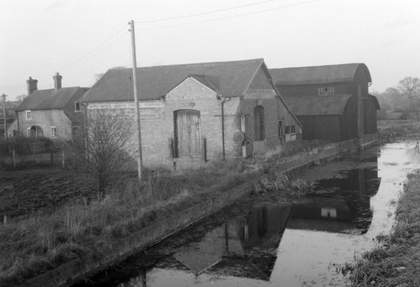 Black and white photograph of a cottage right next to a canal.