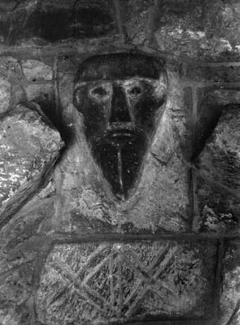 Black and white photograph of a primitive face carved into stone.