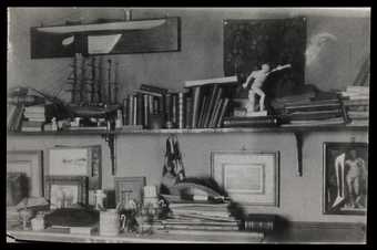 Photograph of a studio with books, prints and an ornament of a man on a shelf