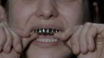 Colour photograph of a woman putting gold teeth in her mouth