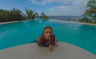 A figure in an infinity pool displays a phone with the image of a woman
