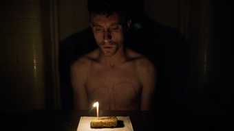 Photograph of a male figure in the dark in front of a cake with candle