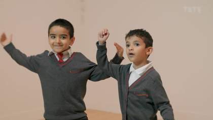 Two boys in school uniform smile while they look at art off camera