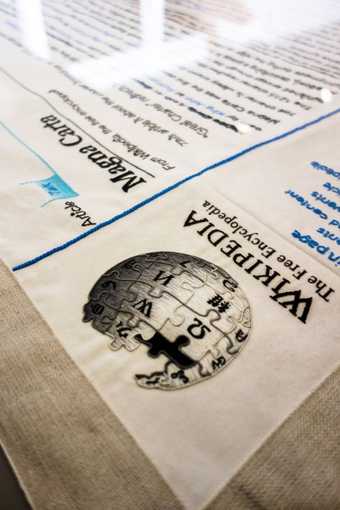 A photograph of an embroidered cloth of Wikipedia's Magna Carta page placed on a wooden table.