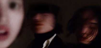 Out-of-focus photograph of three performers' faces in a dark environment
