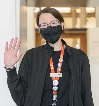 a visitor assistant in a mask stands and waves.