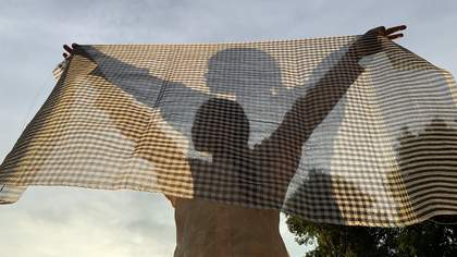 A woman stands behind a thin sheet of material