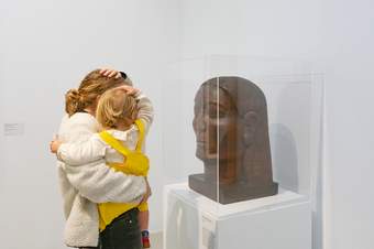 Parent holding toddler looking at a sculpture together in a gallery