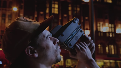 Still form video of artist looking through a camera