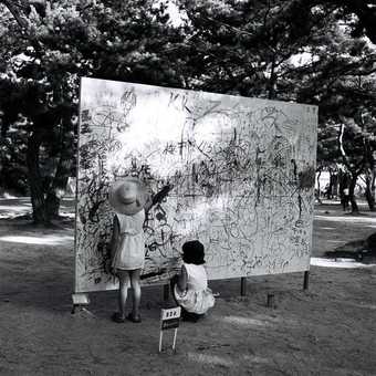 Two girls draw on a board outside in a dense woodland in a park