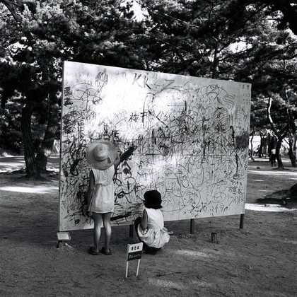 Two girls draw on a board outside in a dense woodland in a park