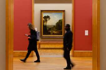 Image of a landscape painting on the wall with two people walking past