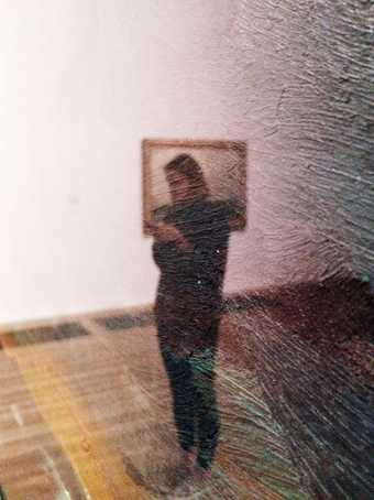 Image taken through a semi-opaque filter blurrily shows a figure standing in a gallery space looking at their phone.