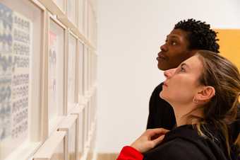 a close up of two people looking a a wall of framed artworks