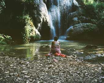 A woman sits in front of a waterfall