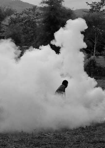Black and white photograph of a person is visable within a cloud of mist in a field