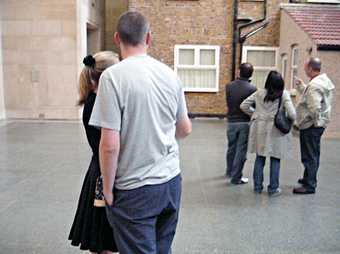 Video still of spectators looking at Michael Landys installation Semi detached at Tate Britain three