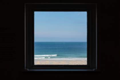 view of a blue sky, sea and sandy beach seen through a square window
