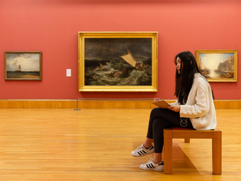 A visitor sitting and drawing in a gallery