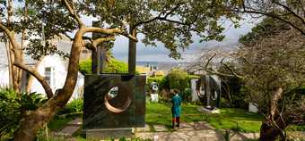 A person in a garden with grass, large trees and large sculptures by Barbara Hepworth