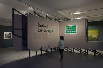 A visitor stands in the exhibition looking at a sign that says 'Radical Landscapes'