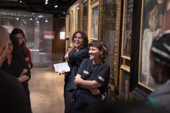 A photograph of two people, Nan and Tabs, laughing as they deliver a talk in the Wellcome Collection gallery.