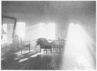 black and white photograph of an empty room with furniture in and an open window