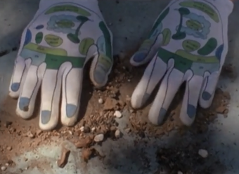 Film still showing gloved hands pressing on earth