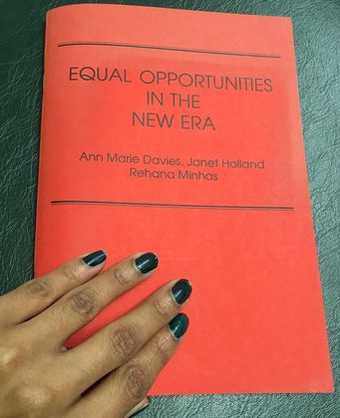 Photograph of a hand with painted nails resting on the cover of a red pamphlet titled Equal Opportunities in the New Era