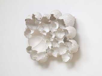 White sculpture made of clustered broken egg shapes against a white background.