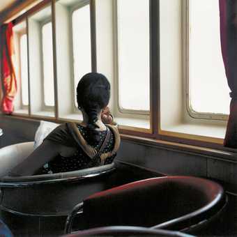 Yto Barrada First class lounge ferry from Tangiers to Algeciras 2002 photograph of a woman sitting in a chair staring out of the ferry window