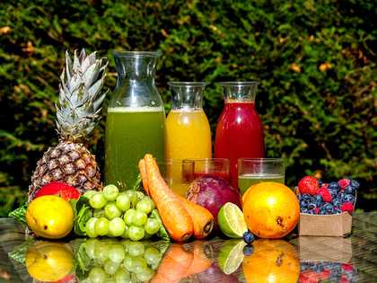 Different sized glass jars filled with smoothies surrounded by fruits and vegetables.