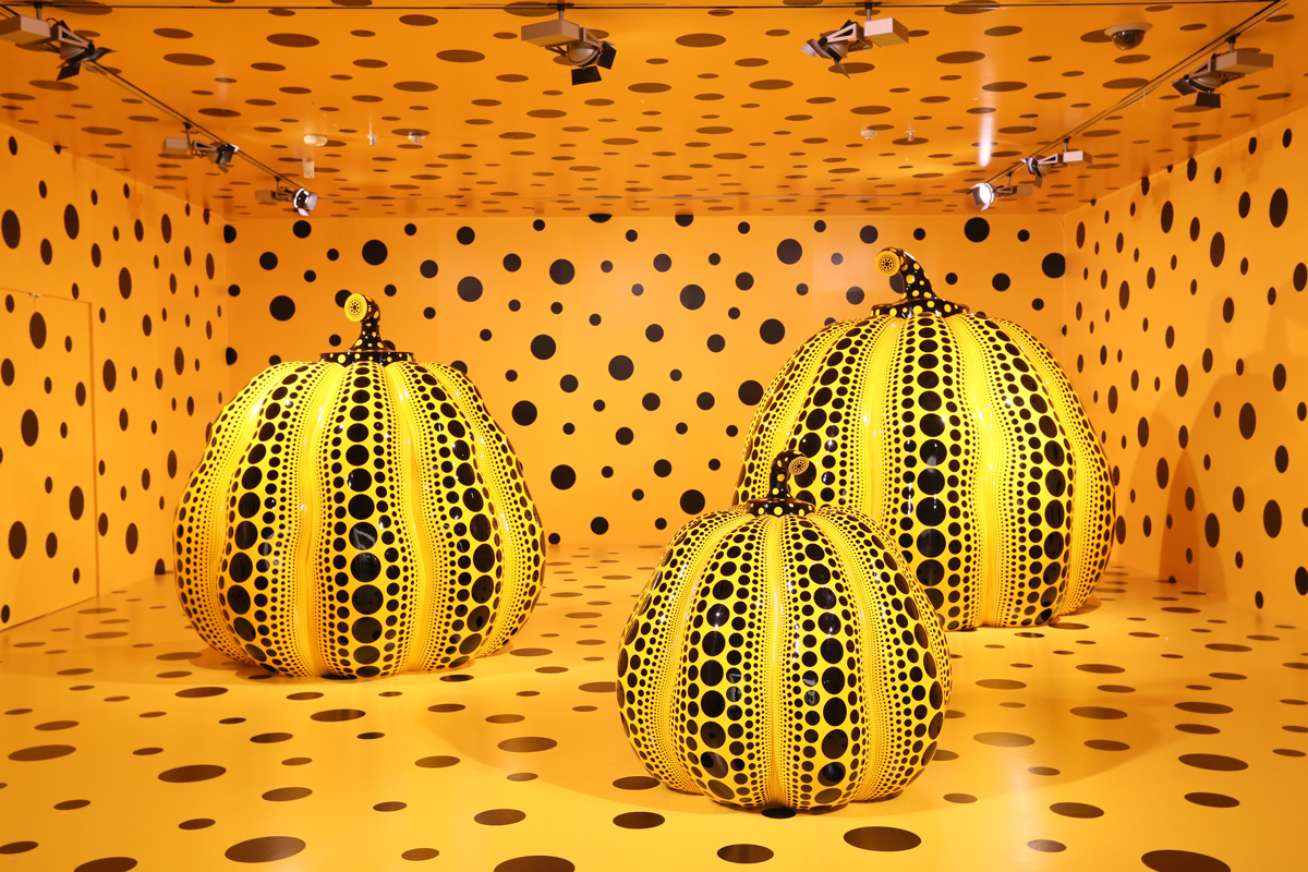 three large yellow pumpkin sculptures sit in a yellow room, covered in spots